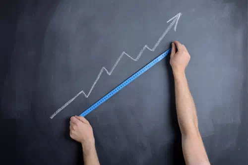 Une personne mesure la courbe de la performance d'une formation management avec un mètre sur un tableau noir